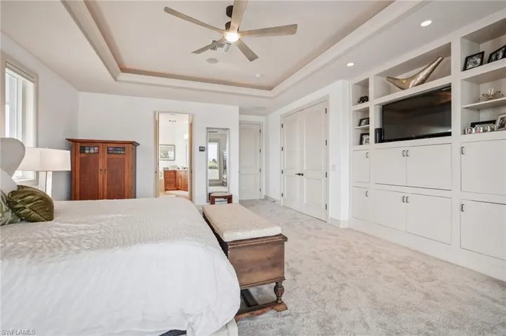 Bedroom featuring a tray ceiling, light colored carpet, ensuite bath, and ceiling fan