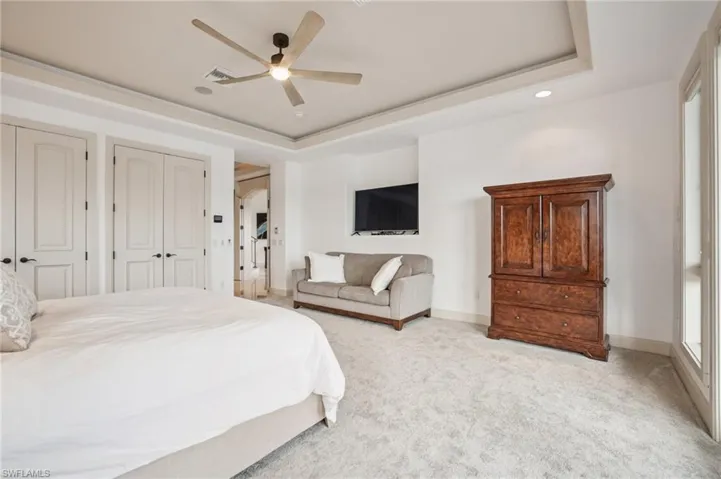 Bedroom with a tray ceiling, light carpet, a ceiling fan, and arched walkways