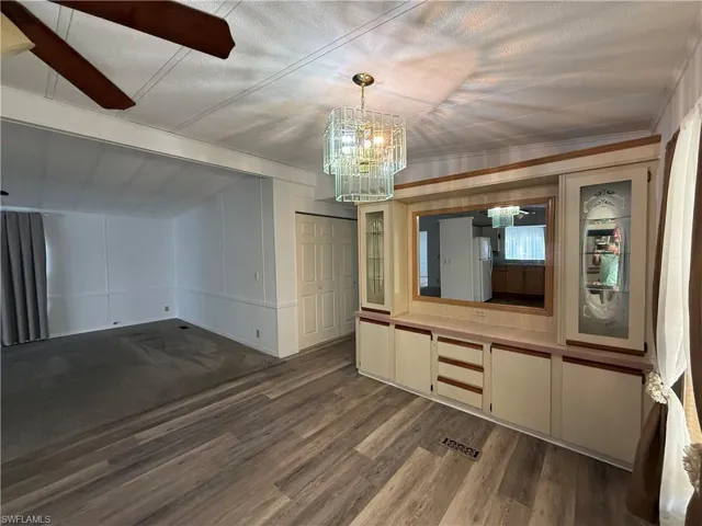 Unfurnished dining area with a decorative wall, dark wood-style floors, a chandelier, and a ceiling fan