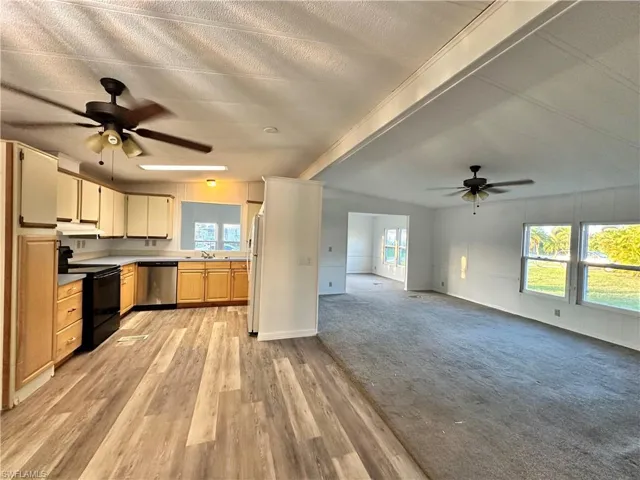 Kitchen with a ceiling fan, black / electric stove, dishwasher, light carpet, and beam ceiling