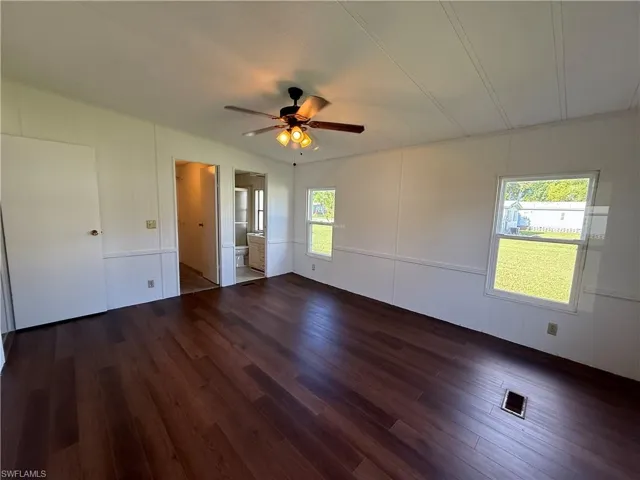 Unfurnished bedroom with dark wood finished floors, a decorative wall, ensuite bathroom, and a ceiling fan