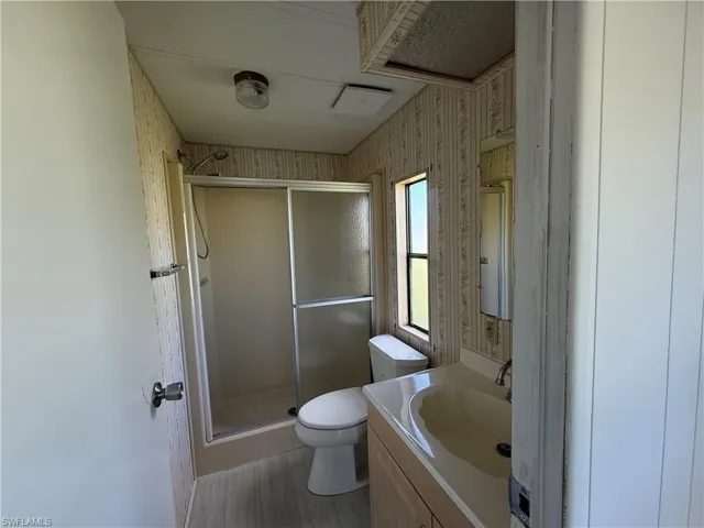Bathroom with a stall shower, vanity, wallpapered walls, and light wood finished floors
