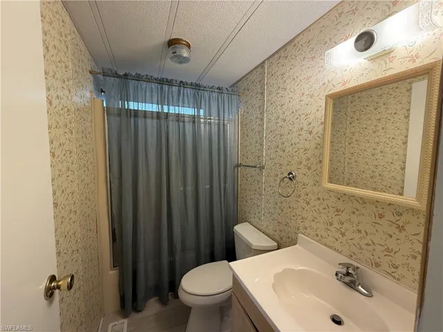 Full bathroom with wallpapered walls, vanity, and a textured ceiling