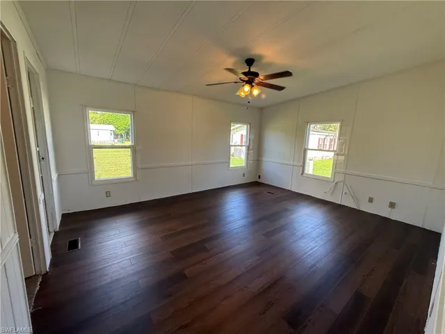 Empty room featuring dark wood-style flooring, ceiling fan, a decorative wall, and wooden walls