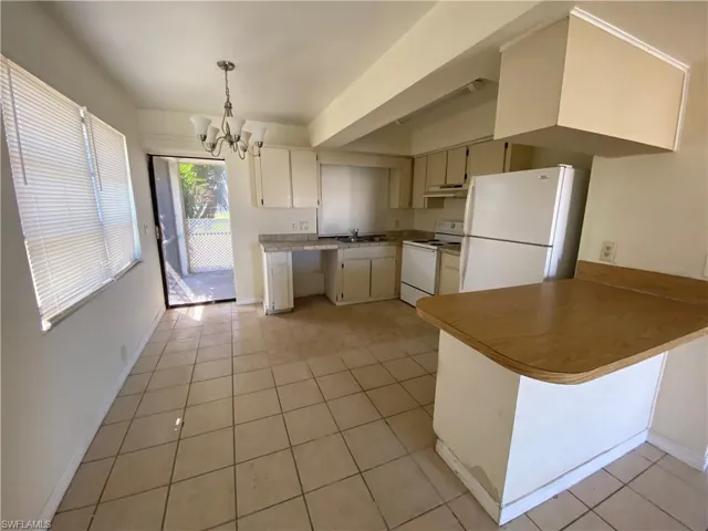 Kitchen featuring white appliances, hanging lights, a peninsula, and light tile patterned floors
