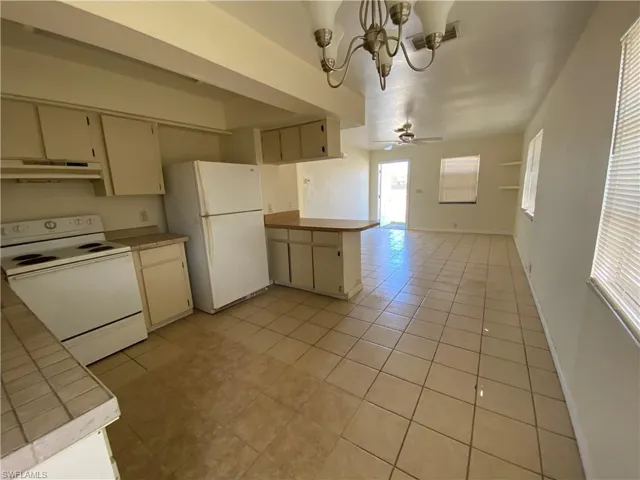 Kitchen featuring white appliances, hanging lights, a peninsula, and light tile patterned floors