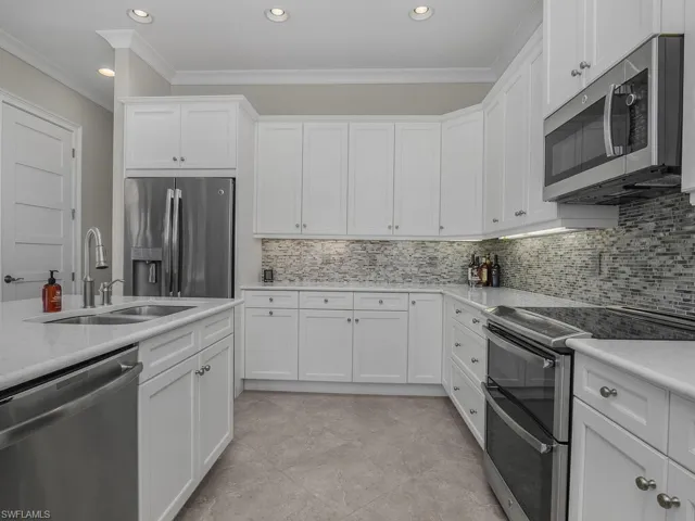 Kitchen with stainless steel appliances, ornamental molding, white cabinets, tasteful backsplash, and recessed lighting. Quartz counter tops.