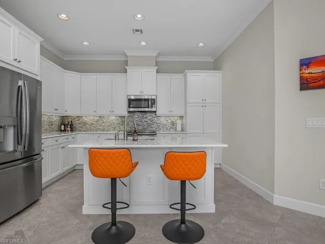 Island Kitchen with stainless steel appliances, backsplash, a breakfast bar, white cabinets, and recessed lighting.
