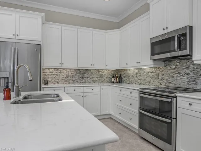 Kitchen with appliances with stainless steel finishes, crown molding, white cabinets, and backsplash, quartz counter tops.