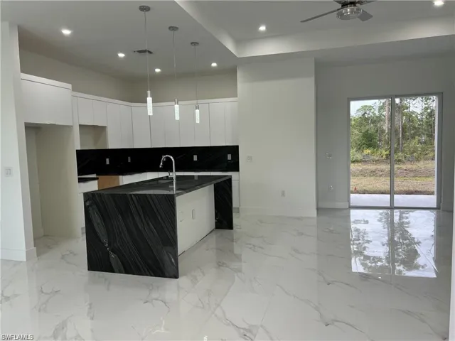 Kitchen with white cabinets, backsplash, ceiling fan, hanging light fixtures, and a center island with sink