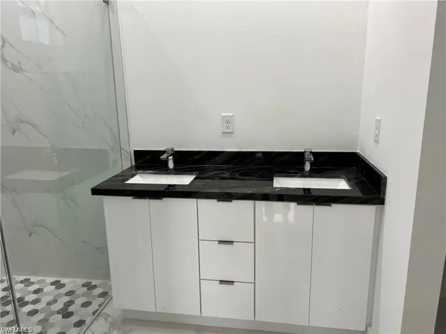 Bathroom with a tile shower, tile patterned flooring, and double vanity