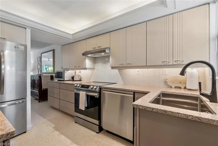 Kitchen with cream cabinetry, decorative backsplash, light stone countertops, stainless steel appliances, and sink