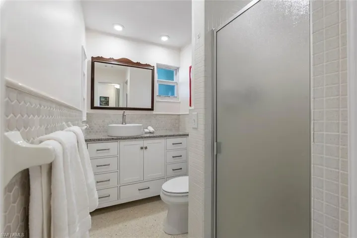 Bathroom with vanity, a shower with shower door, toilet, and tasteful backsplash
