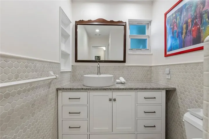 Bathroom featuring vanity, tile walls, toilet, and tasteful backsplash