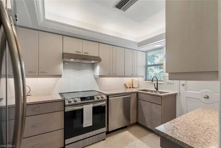 Kitchen with a tray ceiling, appliances with stainless steel finishes, tasteful backsplash, and sink