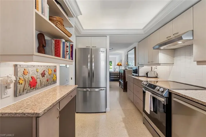 Kitchen with light stone counters, decorative backsplash, a raised ceiling, appliances with stainless steel finishes, and ornamental molding