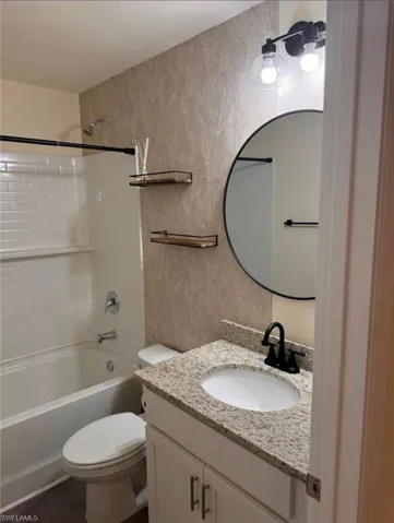 Full bathroom with shower / tub combination, vanity, wallpapered walls, and dark wood-style flooring