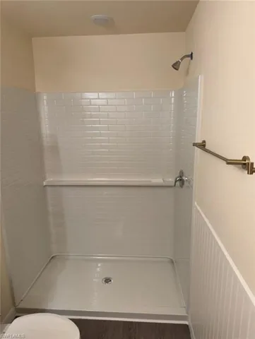 Bathroom featuring a stall shower, dark wood-style floors, and wainscoting