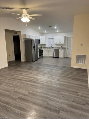 Kitchen featuring stainless steel appliances, open floor plan, white cabinets, vaulted ceiling, and a ceiling fan