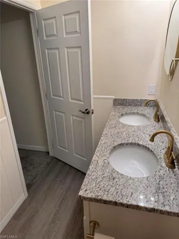 Bathroom with double vanity, dark wood-style flooring, and a wainscoted wall