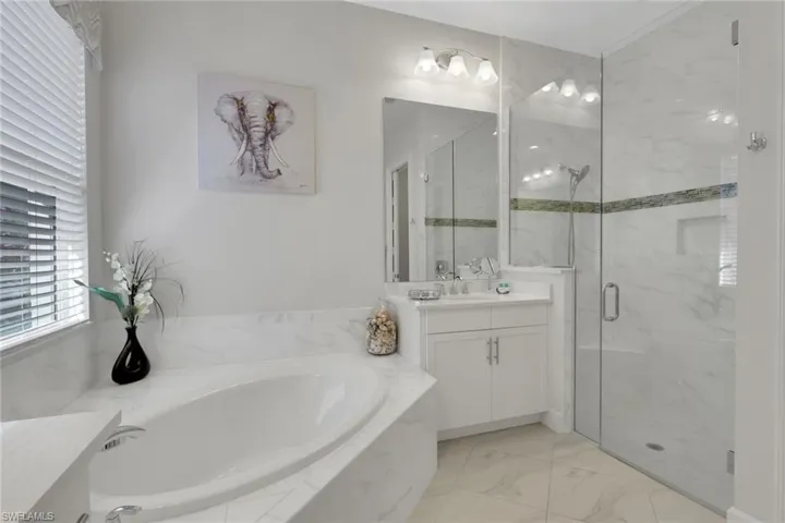 Bathroom featuring vanity, a bath, a marble finish shower, and light marble finish floors