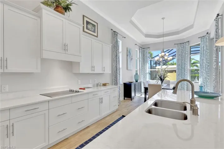 Kitchen featuring white cabinetry, a raised ceiling, light stone counters, light wood-type flooring, and ornamental molding