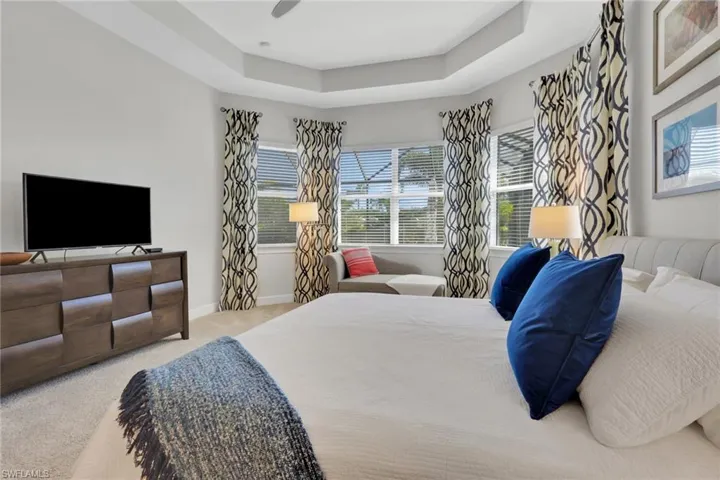 Bedroom featuring a raised ceiling, light colored carpet, and a ceiling fan