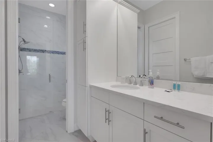 Bathroom featuring vanity, a marble finish shower, and light marble finish floors