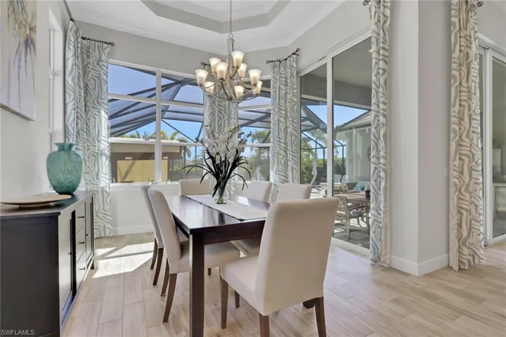 Dining room with a raised ceiling, light wood-style floors, hanging lights, and ornamental molding