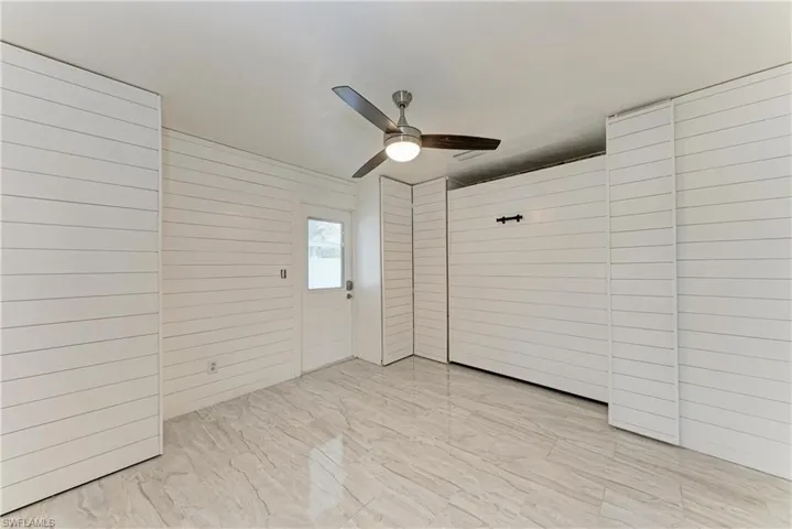 Bedroom with ceiling fan, wood walls, and light marble finish flooring