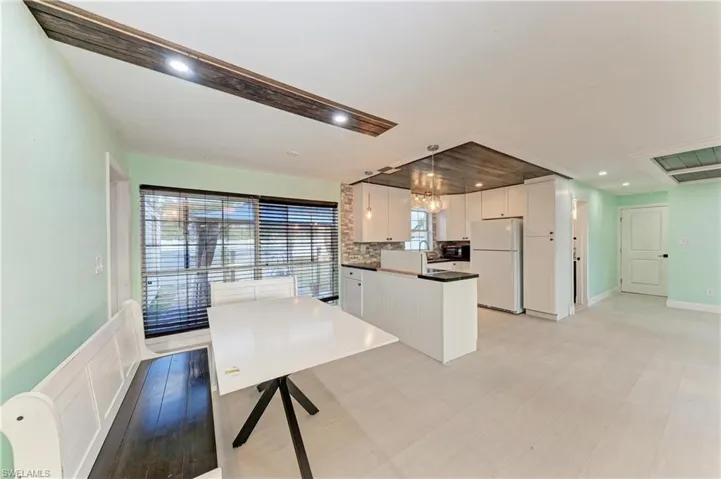 Kitchen featuring dark countertops, white cabinets, freestanding refrigerator, suspended lighting, and a peninsula