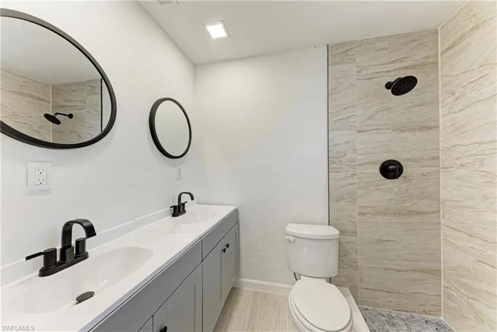 Bathroom featuring a tile shower, double vanity, a textured wall, and light wood-type flooring