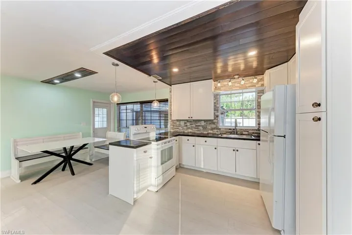 Kitchen featuring dark countertops, a peninsula, white appliances, decorative light fixtures, and white cabinetry
