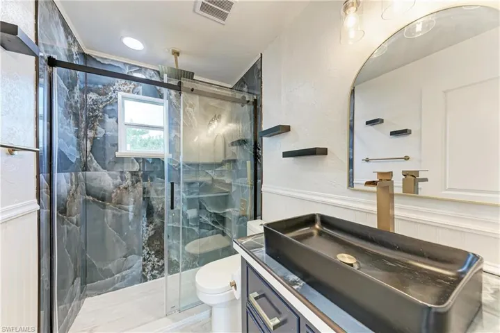 En-Suite Bathroom featuring vanity, wainscoting, and a marble finish shower