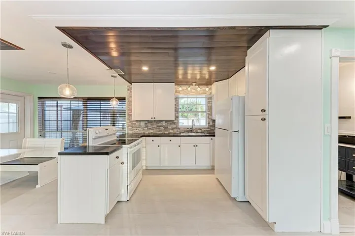 Kitchen featuring white appliances, dark countertops, white cabinets, hanging light fixtures, and tasteful backsplash