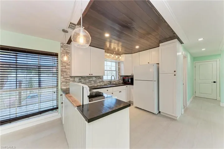 Kitchen featuring freestanding refrigerator, white cabinetry, a peninsula, and range with electric stovetop