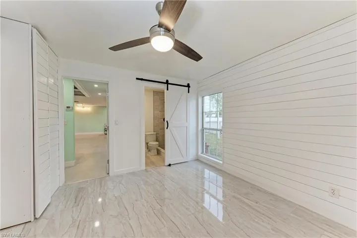 Unfurnished bedroom featuring a barn door, a ceiling fan, ensuite bath, and wooden walls