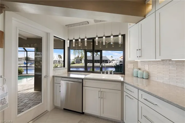 Kitchen featuring stainless steel dishwasher, white cabinets, sink, and a water view