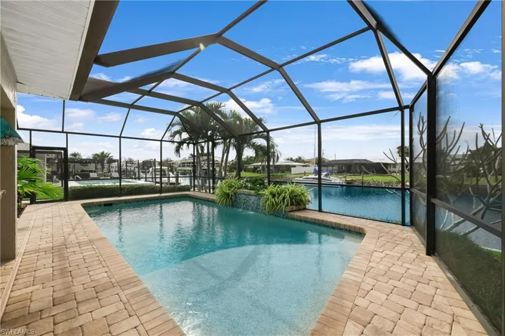 View of pool with glass enclosure, pool water feature, and a patio