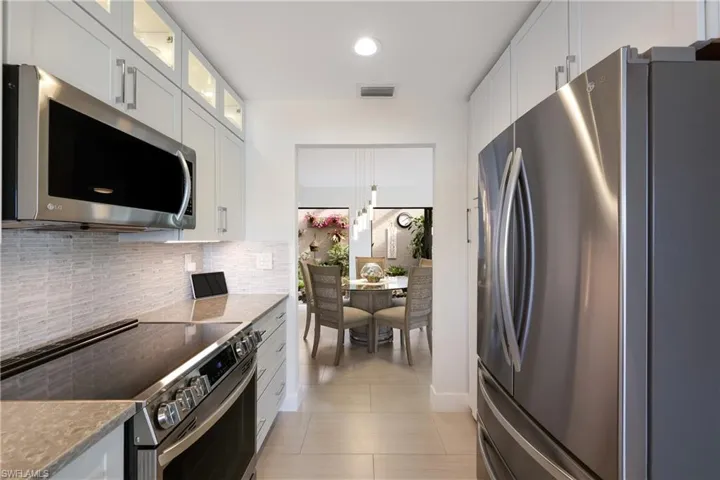 Kitchen featuring decorative backsplash, light countertops, light tile patterned floors, white cabinetry, and stainless steel appliances
