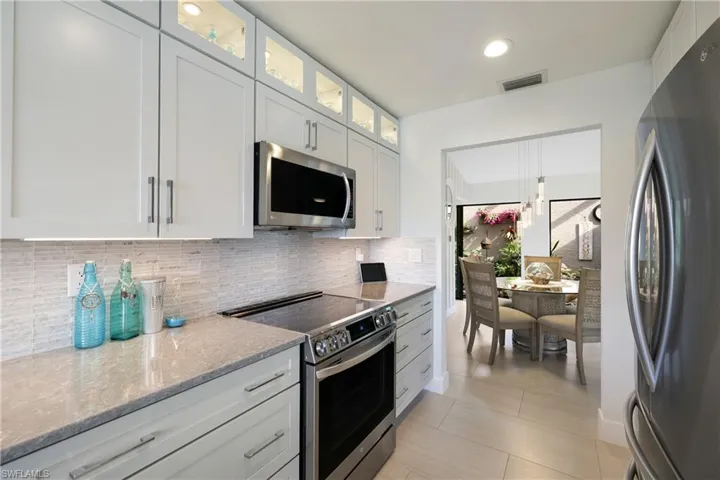 Kitchen with decorative backsplash, light granite counters, stainless steel appliances, pendant lighting, and white cabinets