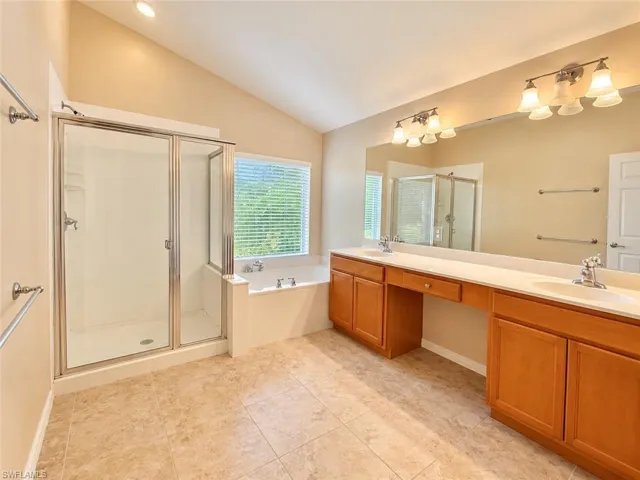 Bathroom featuring a glass-enclosed shower, soaking tub, dual-sink vanity with light-toned cabinetry, and tile flooring under a vaulted ceiling