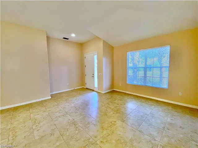Interior space featuring vaulted ceilings, neutral wall tones, large-format tile flooring, and a single-pane exterior entry door with an integrated sidelight