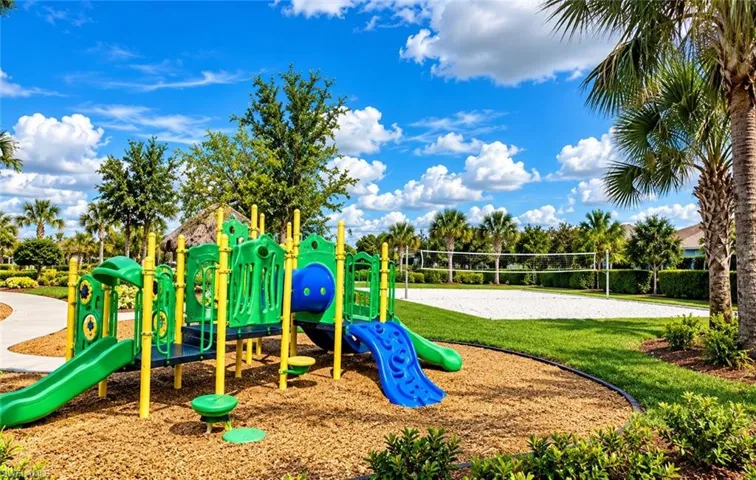 Outdoor recreation area featuring a playground with multiple slides, sand-surface volleyball court, manicured lawn, and mature palm trees