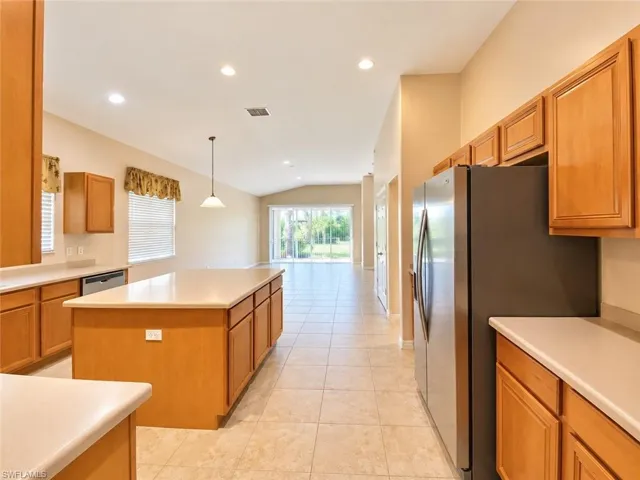 Kitchen featuring light wood cabinetry, stone-finish countertops, central island, stainless steel side-by-side refrigerator, and tile flooring
