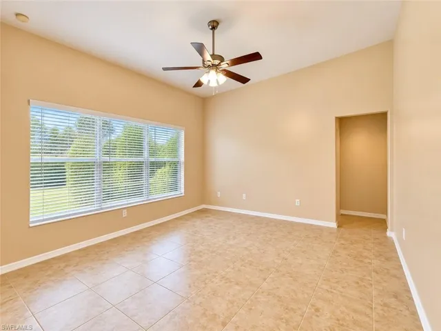 Vaulted ceilings featuring a multi-blade ceiling fan with integrated lighting, expansive window with horizontal blinds, and neutral-toned ceramic tile flooring