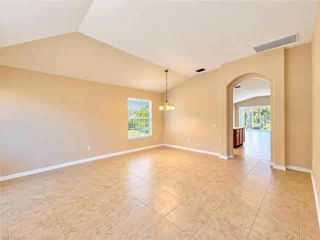 Vaulted ceilings, large-format tile flooring, a multi-pane window, a hanging chandelier, and an arched architectural opening