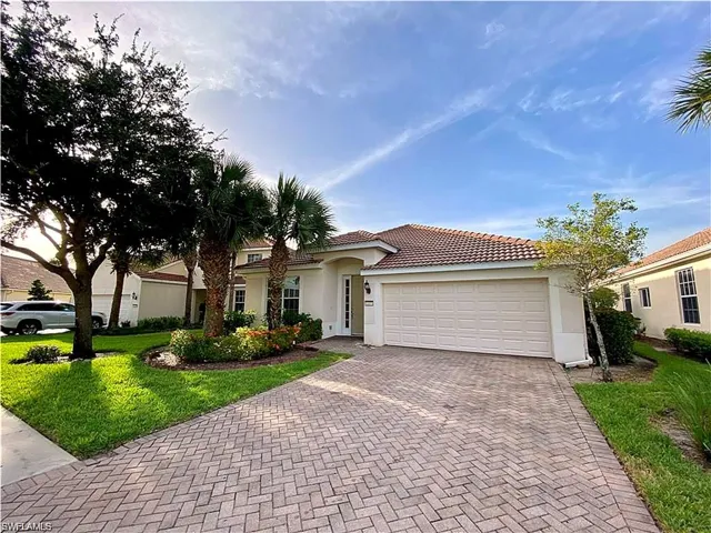 Stucco exterior featuring a tiled roof, paver driveway, two-car garage, and established landscaping