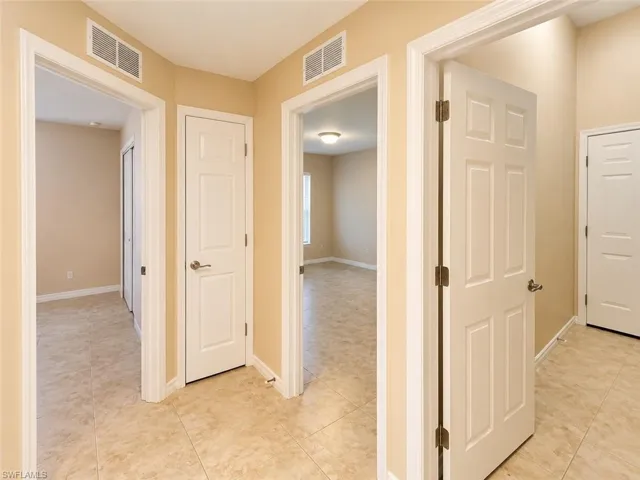 Neutral-toned interior hallway featuring tile flooring, six-panel interior doors, and crisp white door trim