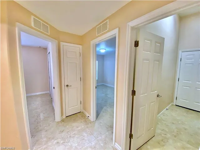 Interior hallway featuring neutral-toned tile flooring and six-panel interior doors with brushed nickel hardware